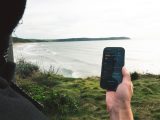 Person holding phone overlooking ocean and beach