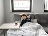 A woman rests on a couch indoors, feeling unwell, with a cup of tea nearby.