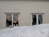 a white house with two windows and a pile of snow