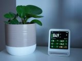 Air quality monitor next to a potted plant on a desk, showing CO2 and PM2.5 levels.