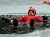 Adult male practicing ice rescue techniques in a red survival suit on frozen lake.