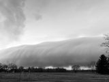 A dramatic shelf cloud hangs over a rural landscape.