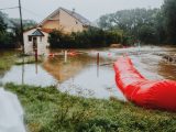 Flooded residential area protected by red flood barriers, showing severe weather impact.