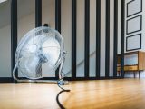 A sleek electric fan placed on a wooden floor in a modern indoor setting, providing comfort and cooling.