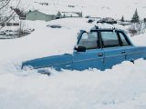 A blue car buried in deep snow.
