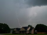 A vivid lightning bolt pierces the sky over suburban houses during a storm, capturing nature's raw power.