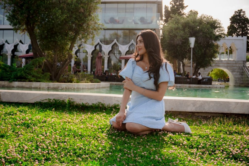 Young woman in a light blue dress sitting on grass.