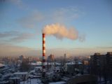 Smoke stack emitting steam in an urban winter landscape at sunrise.