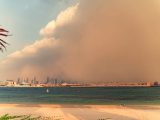 A dramatic sandstorm approaches the Dubai skyline over the calm sea, creating a striking contrast.