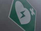 Green first aid sign featuring a broken heart and cross symbol for medical emergency awareness.