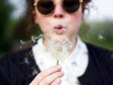 Close-up of a woman blowing a dandelion outdoors, symbolizing freedom and wishes.