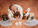 Newborn baby sleeps in tiny chair with money props.