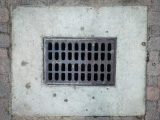 A grate on the side of a brick wall
