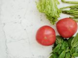 Close-up of fresh vegetables including tomatoes, basil, lettuce, and asparagus on marble.