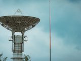 Large satellite dish tower standing tall under a cloudy sky.
