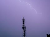 A striking image of lightning illuminating the sky above a cell tower, captured at night.