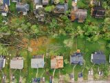 Drone dramatic view of small settlement cottages with ruined roofs and windthrown trees after massive storm