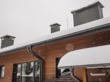 A close-up of a snow-covered roof with chimneys during winter snowfall, highlighting winter architecture.