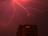 Intense lightning bolts illuminate the night sky above a city building, showcasing a thrilling weather phenomenon.