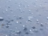 Close-up view of frozen hailstones scattered on icy pavement, showcasing winter weather phenomena.