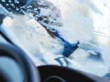 Hand scraping ice off a car windshield during a cold winter morning.