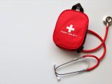 Red first aid kit and stethoscope on a white surface, ideal for healthcare themes.