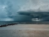 A powerful storm approaches a serene sandy beach with dramatic clouds and turbulent waves.