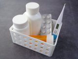 Healthcare basket with medication bottles, pills, and thermometer on a dark surface.