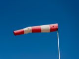 Vibrant red and white windsock blown by the wind against a clear blue sky.