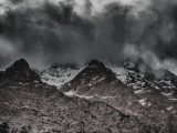 Majestic snow-capped mountain peaks shrouded by dark storm clouds, creating a dramatic and moody landscape view.