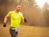Fit adult man running in a cross country race wearing neon sportswear and gloves, captured in motion outdoors in Brașov.
