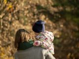 A loving mother carries her child through a picturesque autumn park in Poland.