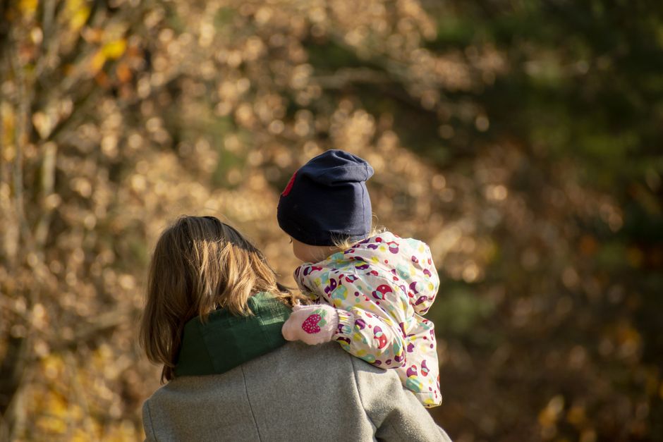 A loving mother carries her child through a picturesque autumn park in Poland.