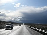 Highway scene under a dramatic sky with storm clouds and two cars, offering a sense of adventure.