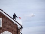 A man shoveling snow off a rooftop, indicating winter outdoor activity.