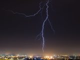 A striking lightning bolt illuminates a bustling cityscape under the night sky.