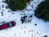Drone shot of people camping in a snowy forest with a campfire and car.