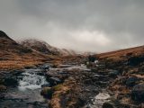 a man walking across a stream in the mountains