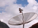 Silver satellite dish pointing skyward under a bright blue sky with scattered clouds.