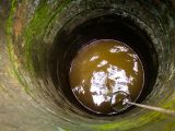 A view down an old stone well showing murky water and a rope with a bucket.