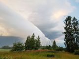 Stunning shelf cloud formation hovering over a peaceful, lush green field and forest landscape.