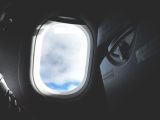 Silhouette of a passenger looking through an airplane window at the clouds outside.