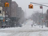 A snow-covered urban street with traffic lights and a lone pedestrian, capturing the essence of winter in the city.