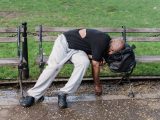 A man resting on a bench outdoors with a backpack, suggesting themes of homelessness and urban life.