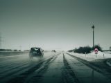 Car driving through snowy highway with fog, creating a mysterious atmosphere.