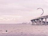Kitesurfer enjoying the ocean near a modern bridge on a cloudy day.