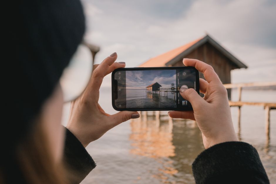 A person captures a picturesque lakeside house in Bavaria on their smartphone.