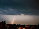 Stormy evening with a dramatic lightning strike illuminating the cityscape below dark clouds.