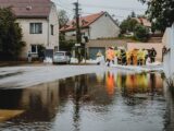 Emergency workers in rain gear manage floodwaters in a suburban street.