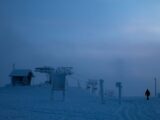 Silhouetted person walking in snowy winter landscape with frosted cable cars.